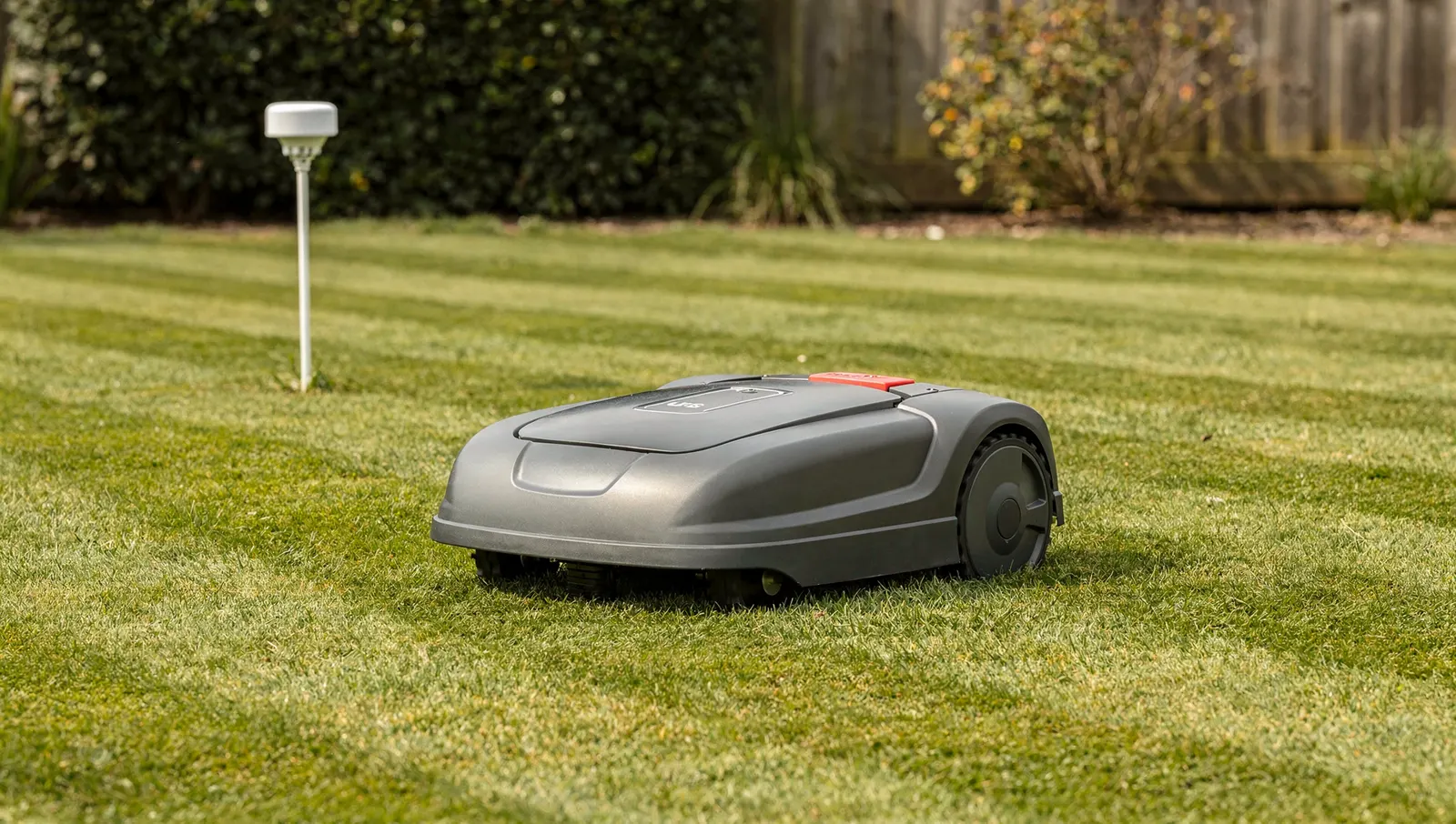 Robot tondeuse sur une pelouse rayée, petite antenne GPS dans un coin du jardin